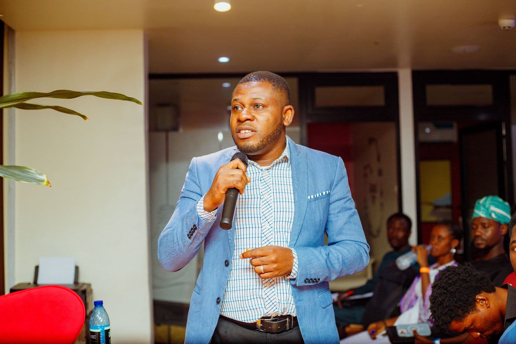 A speaker in a light blue blazer addresses the room